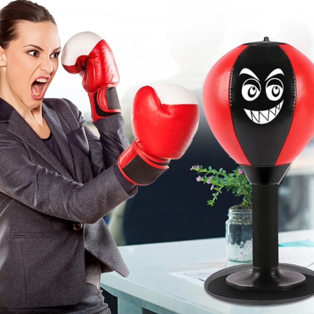 Woman in a gray suit with red boxing gloves punching a black and red punching bag with a face design.